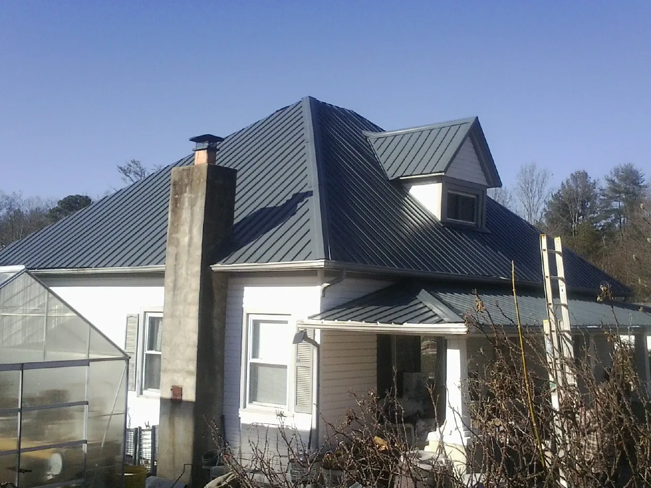 Dark blue standing seam metal roof on a white farmhouse with dormer — Slate & Tile Roof Repair by Roofing Brothers in Fayette